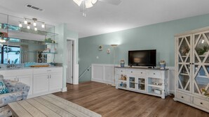 A spacious living room with a wooden floor, a ceiling fan, a television, and a cabinet with glass doors.
