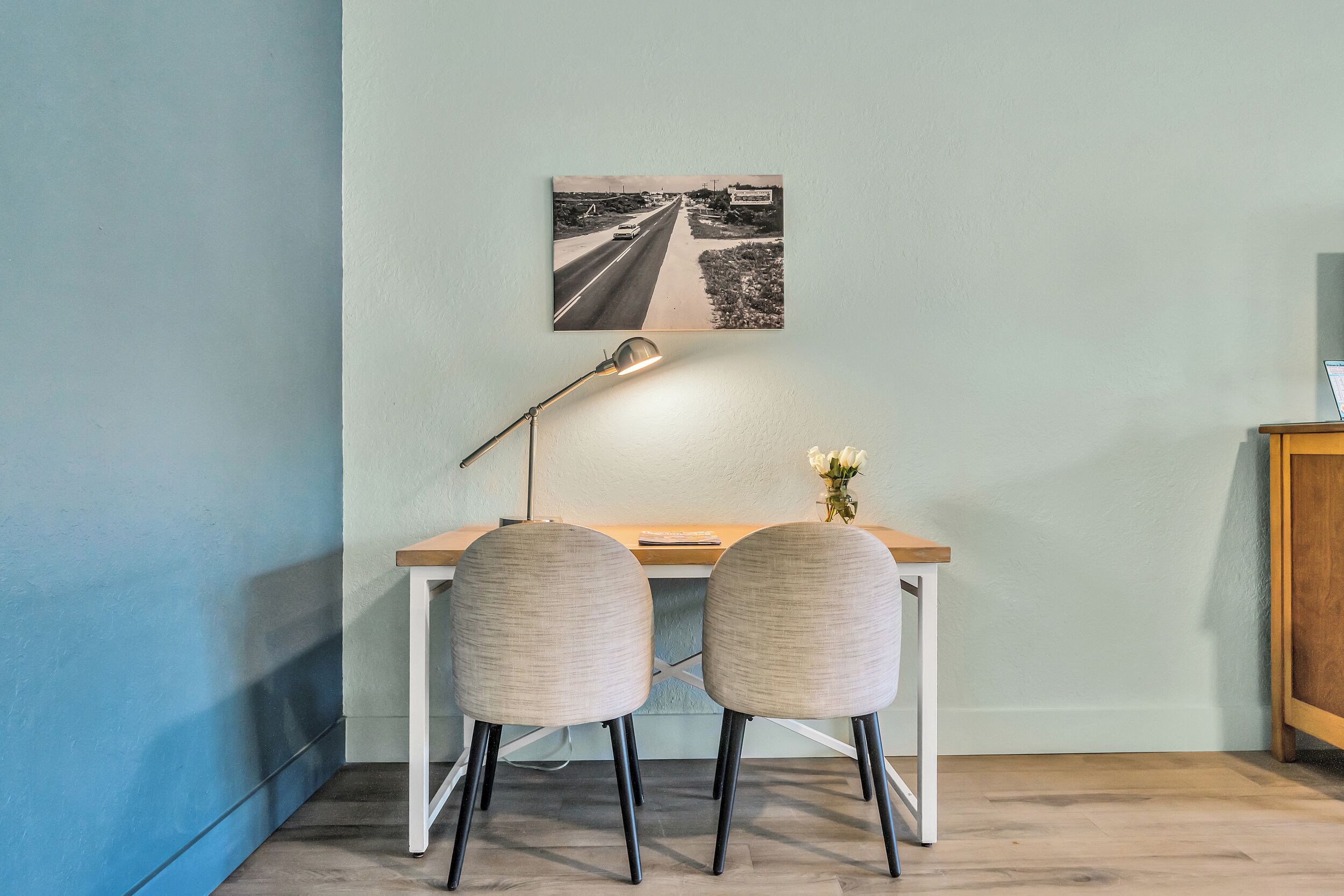 A room with a desk, two chairs, a lamp, and a framed picture on the wall.