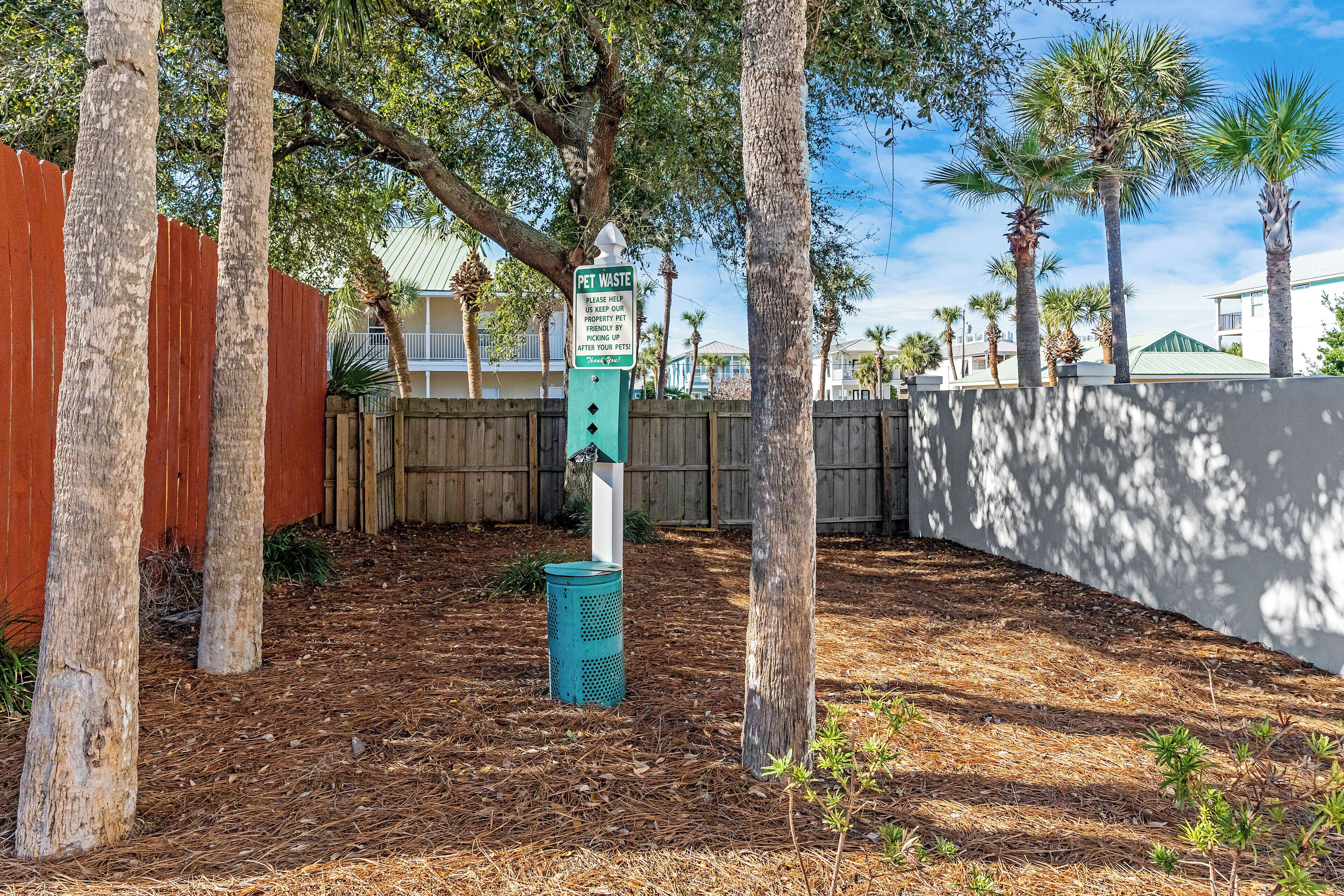 A fenced backyard with a pet waste sign, trees, and a wooden fence.