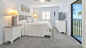 Ein Schlafzimmer mit einem Bett, zwei Nachttischen mit Lampen, einem Deckenventilator, einem Fernseher auf einer Kommode und einem Balkon mit Blick.