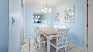 Ein Essbereich mit einem Holztisch und weißen Korbstühlen, hellblauen Wänden und einer Deckenleuchte.
