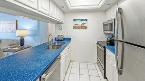 Eine moderne Küche mit weißen Schränken, einer blauen Arbeitsplatte, Edelstahlgeräten und einem Deckenventilator.