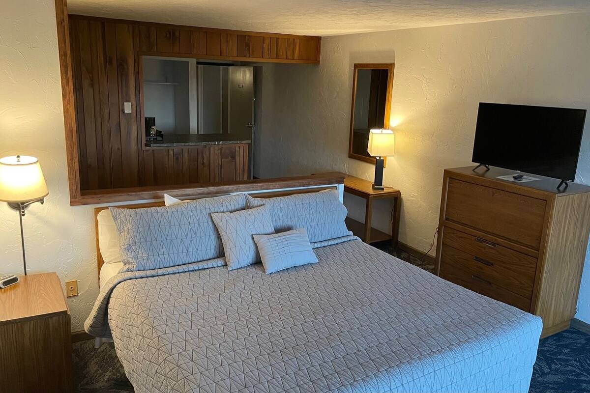 Una habitación de hotel con cama, televisión, cómoda, espejo y lámpara.