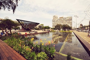 A public square with a modern sculpture, a water feature, and surrounding greenery.