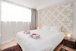 Una camera d'albergo con un letto grande, due cuscini, un comodino con una lampada e carta da parati decorata.