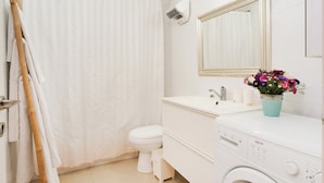 A bathroom with a shower curtain, toilet, sink, mirror, and a washing machine. - Stylish 1BR with Balcony — Steps to Beach & City (Tel Aviv-Yafo)