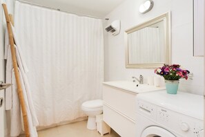 Un bagno con tenda da doccia, WC, lavandino, specchio e lavatrice.