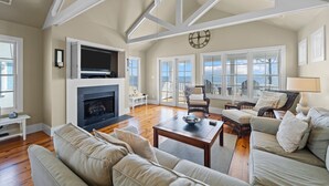 A spacious living room with a fireplace, comfortable seating, and large windows offering a view of the outdoors. - Neuse Village #5 - Quaint, tranquil cottage with pool & amazing views (Arapahoe)