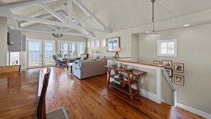A spacious living area with a wooden floor, a large sofa, a dining table, and a staircase with a railing. - Neuse Village #5 - Quaint, tranquil cottage with pool & amazing views (Arapahoe)
