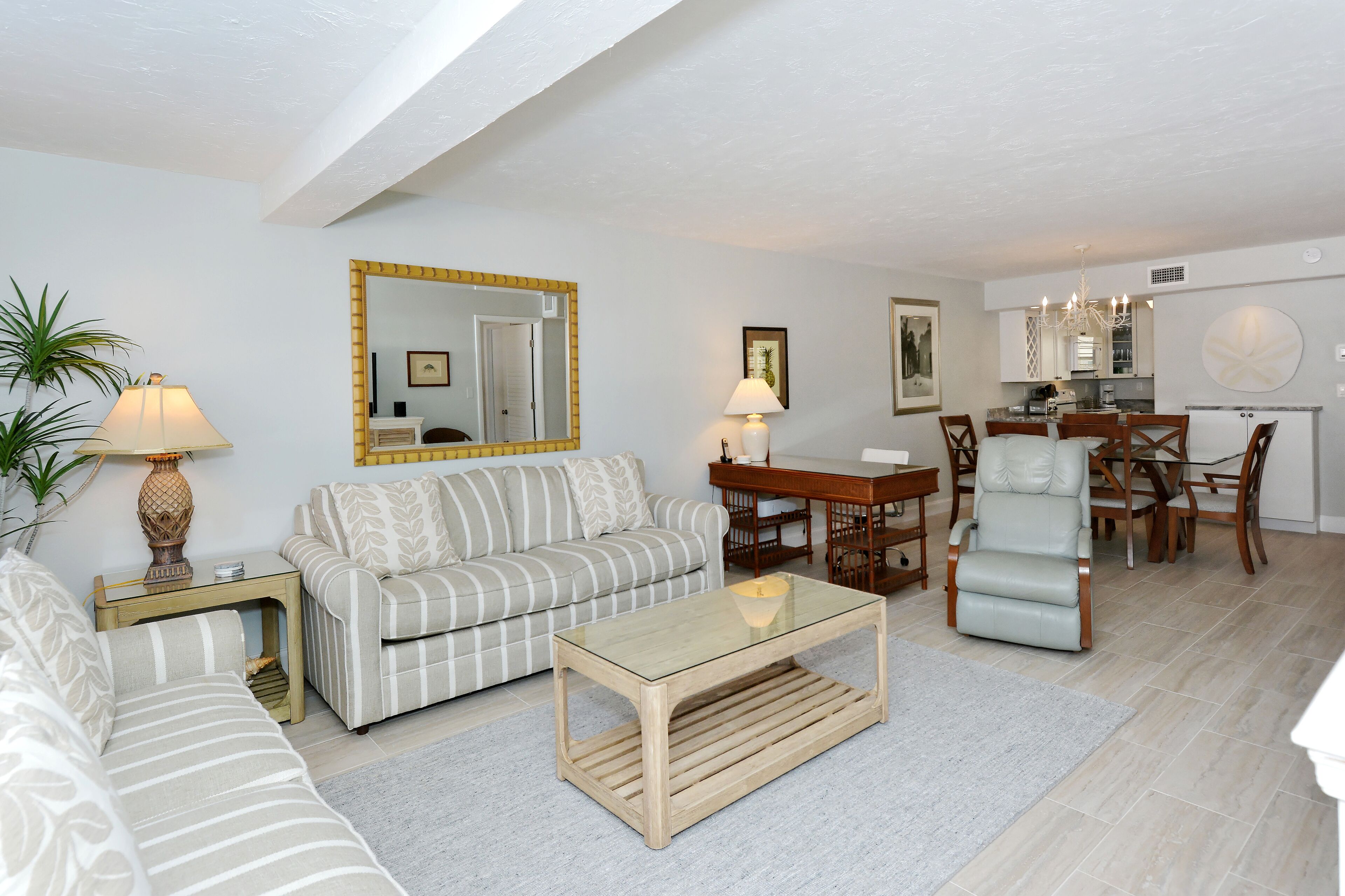 A living room with a sofa, a coffee table, a dining table with chairs, and a kitchen area in the background.