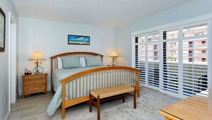 A bedroom with a wooden bed, two bedside tables with lamps, a bench, a large window with blinds, and a painting on the wall.
