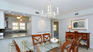 A modern kitchen with a central island, a dining area with a glass table and wooden chairs, and a chandelier.