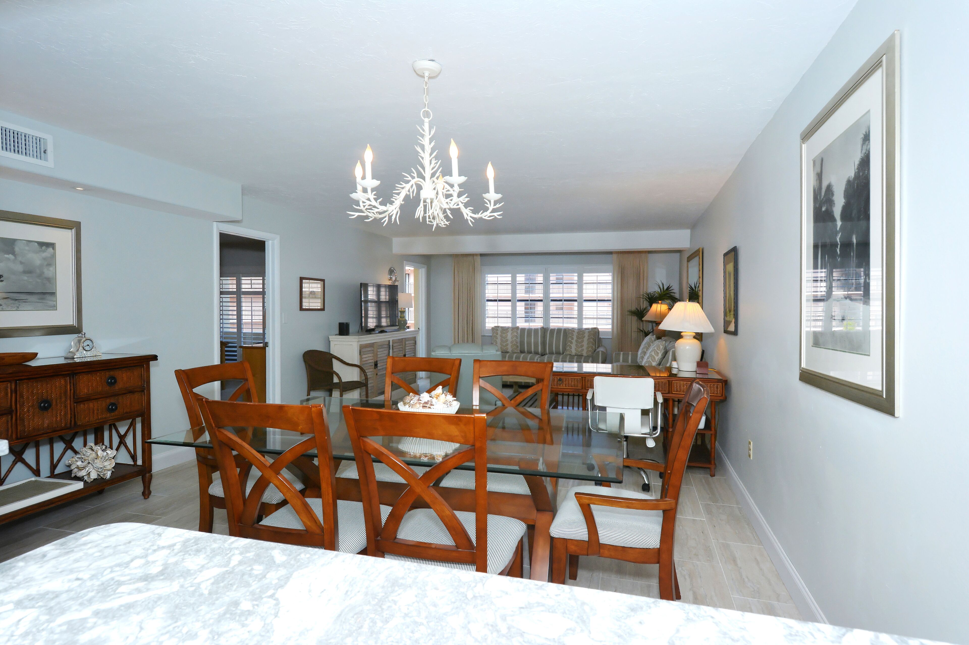 A dining area with a glass-top table, wooden chairs, a chandelier, and framed artwork on the walls.