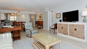 A living room with a glass-top coffee table, a sofa, a dining table with chairs, a television, and a cabinet.