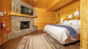 Ein gemütliches Blockhaus-Schlafzimmer mit Kamin aus Stein, einem Bett mit blauer Decke und Holzboden.