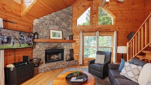 Ein gemütliches Blockhaus-Interieur mit Kamin aus Stein, Holzwänden, einer bequemen Couch und einem wandmontierten Flachbildfernseher.
