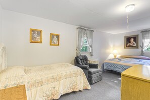 Une chambre avec deux lits, une chaise, une commode en bois et trois tableaux encadrés accrochés au mur.