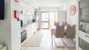 A modern kitchen with white cabinets, a stainless steel sink, and a dining area with a table and chairs. - Flat Praia Rocha Sea View Sand (Portimão)