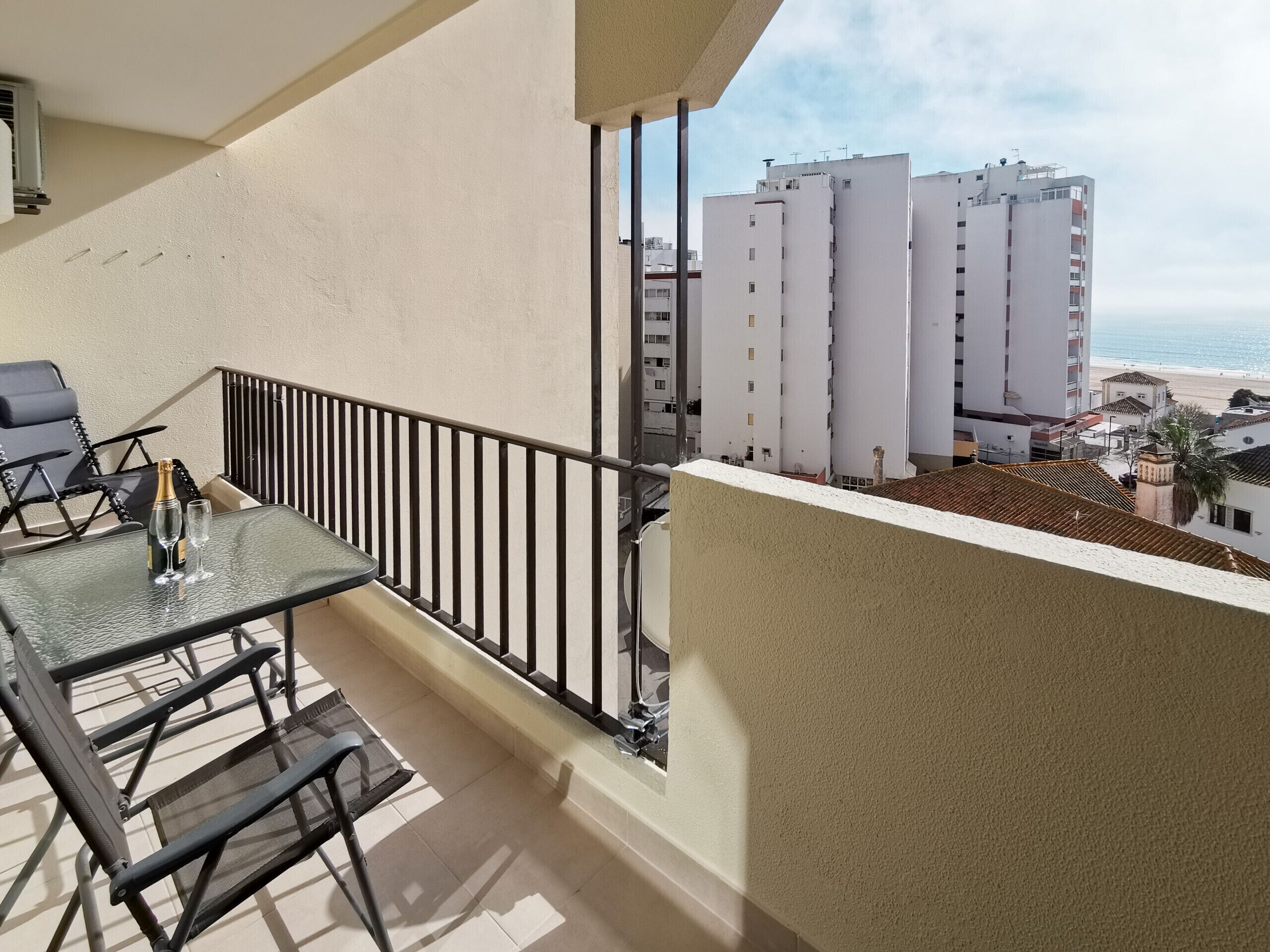A balcony with a table and chairs, overlooking a beach and buildings.