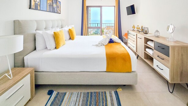 A modern hotel room with a large bed, a desk, a TV, and a balcony view. - Flat Praia Rocha Sea View Sand (Portimão)
