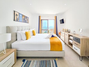 A modern hotel room with a large bed, a desk, a TV, and a balcony view. - Flat Praia Rocha Sea View Sand (Portimão)