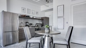 A modern kitchen with a stainless steel refrigerator, a round dining table with chairs, and a potted plant. - Ponce City Market Studio · Heart of Atlanta · BeltLine (Atlanta)