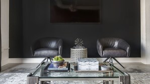 A modern living room with two black leather chairs, a glass coffee table, and a black wall with a framed picture. - Ponce City Market Studio · Heart of Atlanta · BeltLine (Atlanta)
