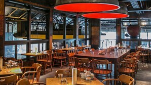 A modern restaurant with high ceilings, exposed beams, and large windows. Tables are arranged in a spacious layout with orange chairs. - Ponce City Market Studio · Heart of Atlanta · BeltLine (Atlanta)