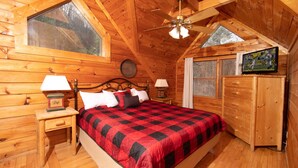 A cozy wooden cabin bedroom with a large bed, a nightstand with lamps, a dresser, and a ceiling fan. - Private Cabin, Hot Tub, Pool Table, Walking Distance to Fishing Pond (Sevierville)