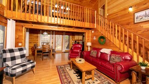 A wooden cabin interior with a dining area, a red leather sofa, and a checkered armchair. - Private Cabin, Hot Tub, Pool Table, Walking Distance to Fishing Pond (Sevierville)