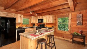 Cocina de estilo cabaña con encimera central, taburetes de bar y refrigerador.