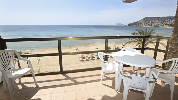 Varanda com vista para a praia, cadeiras de plástico branco e uma mesa.