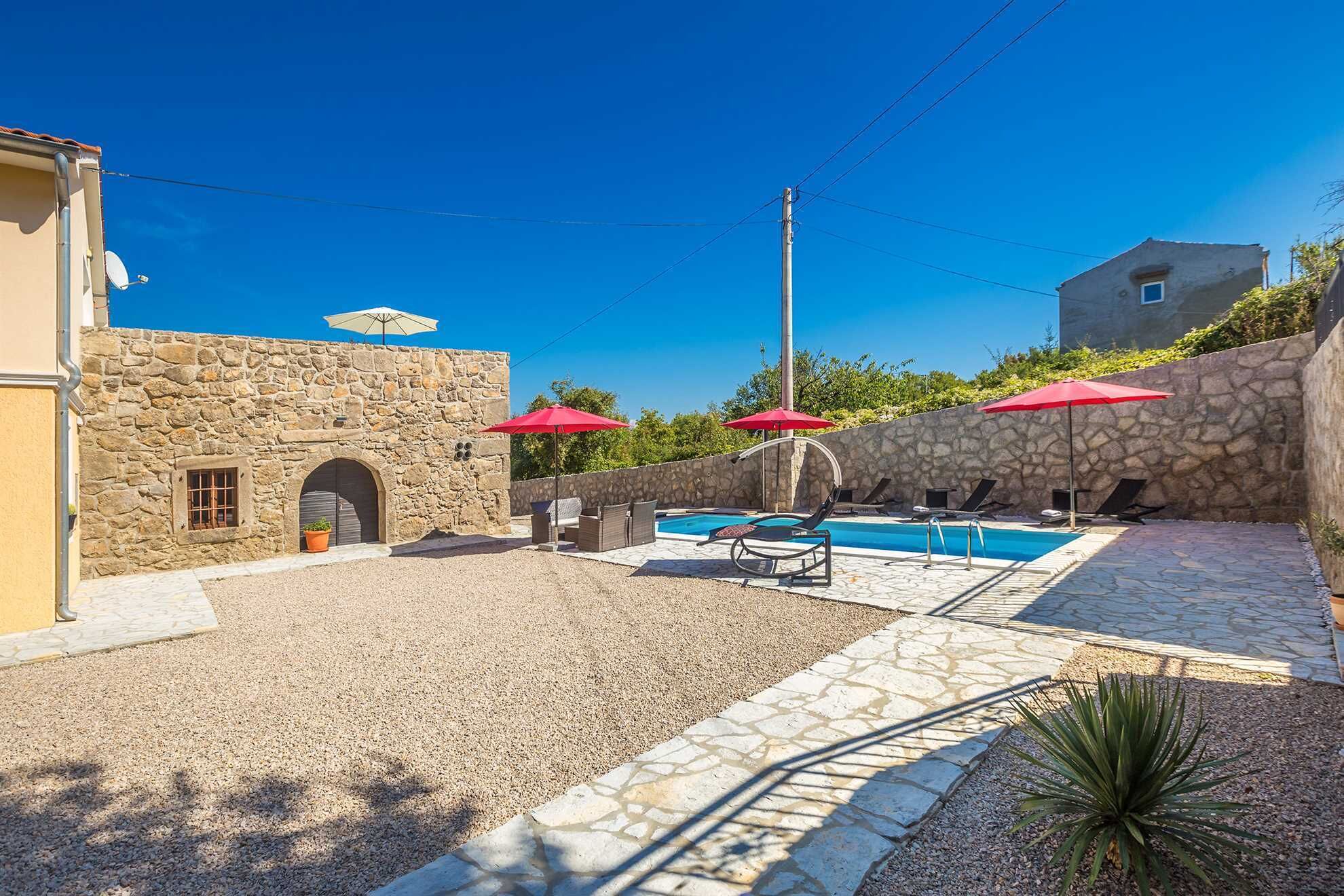 A stone building with a pool area, including lounge chairs and umbrellas.