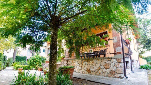 Un bâtiment en pierre doté d’un balcon, entouré d’une végétation luxuriante et agrémenté de plantes en pot.