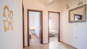 Un couloir au plancher de bois menant à une chambre à coucher équipée d’un lit et d’une table de chevet.