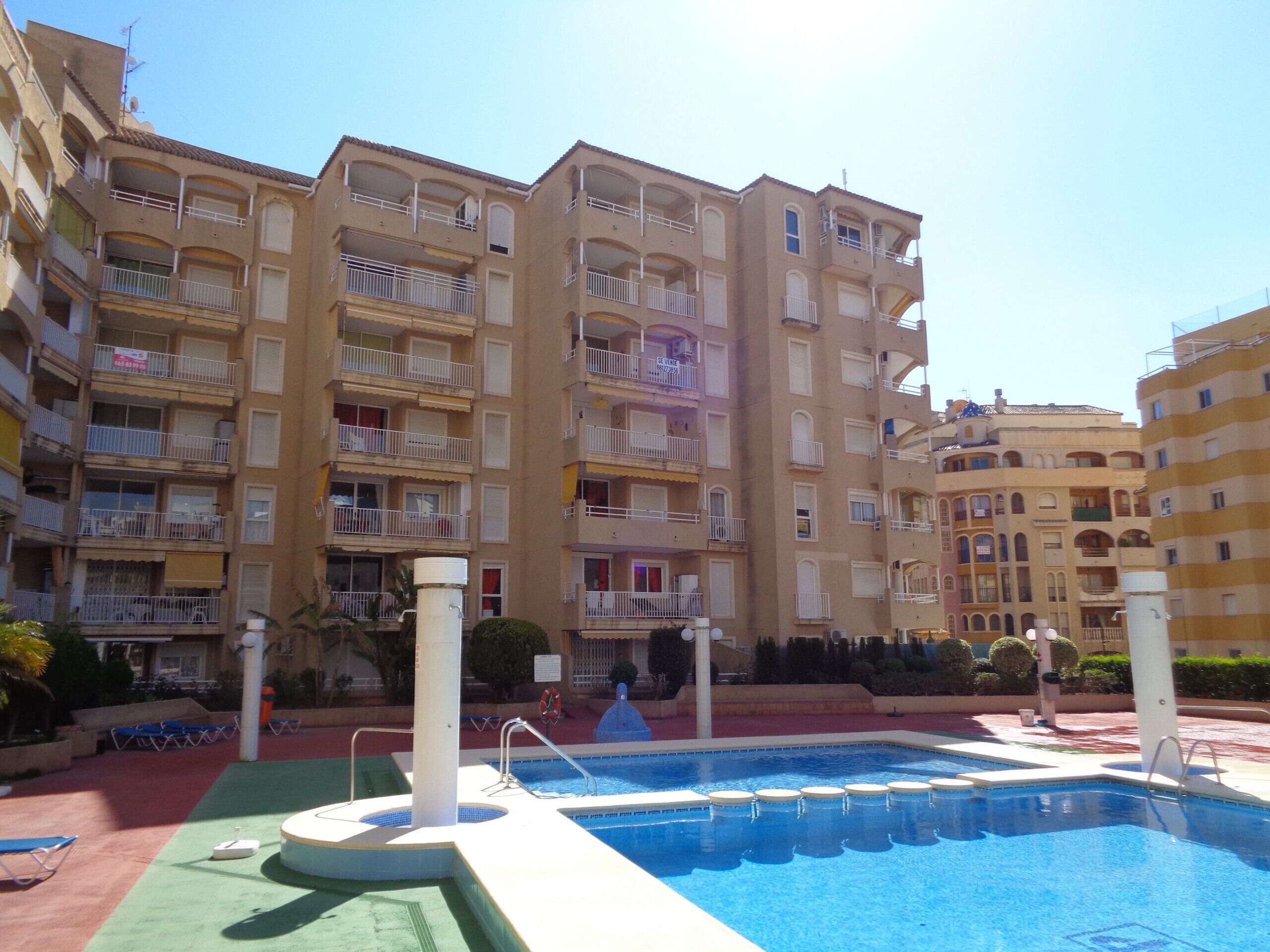 Un immeuble résidentiel à plusieurs étages doté de balcons, d’une piscine et d’un espace extérieur verdoyant avec des chaises longues.