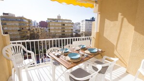 Un balcon avec une table en bois prévue pour quatre personnes, des chaises en plastique blanches et un auvent jaune.