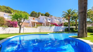A swimming pool with a curved edge, surrounded by a white wall and lush greenery. - Apartment with Pool in Cala Crancs area · UHC CASAS BLANCAS 121 (Salou)