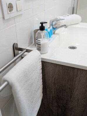 Une salle de bain avec un lavabo blanc, un porte-serviettes, un distributeur de savon et un miroir.