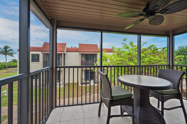A covered balcony with a table and chairs, a ceiling fan, and a view of a building with red roofs.