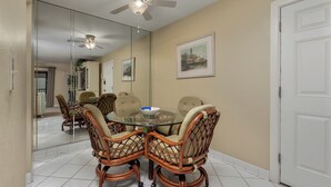 A dining area with a glass table surrounded by wicker chairs, a ceiling fan, and a door on the right. - Partial Beach View 2 bed, 2 bath at Sanibel Moorings #742 (Sanibel)