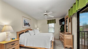 A bedroom with a bed, bedside tables, a dresser, a ceiling fan, a TV, and a window with blinds. - Partial Beach View 2 bed, 2 bath at Sanibel Moorings #742 (Sanibel)