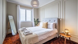 A neatly arranged bedroom with a large bed, a bedside table with a lamp, a mirror, and a window with curtains. - Sea View - By WeHostMadeira (Câmara de Lobos)