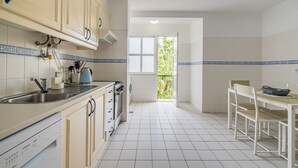 A kitchen with white cabinets, a sink, a stove, and a dining area with a table and chairs. - Sea View - By WeHostMadeira (Câmara de Lobos)