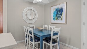 Un coin repas avec une table bleue et des chaises blanches, un élément décoratif mural et un tableau abstrait encadré.