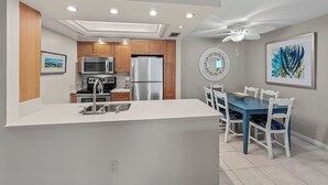 Une cuisine moderne dotée d’un îlot central, d’appareils électroménagers en acier inoxydable et d’un coin repas avec une table bleue et des chaises blanches.