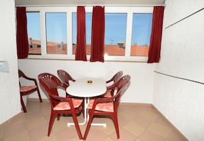 A small balcony with a table and chairs, a window with curtains, and a view of buildings. - Apartment Filipin in Porec, Istria (Porec)