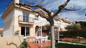 Un edificio de dos pisos con un balcón, un patio con mobiliario exterior y un área de jardín.
