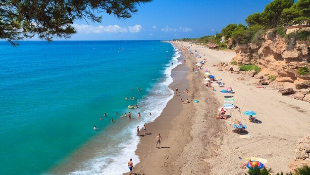 Una playa con aguas turquesas cristalinas, una orilla arenosa y numerosas sombrillas.