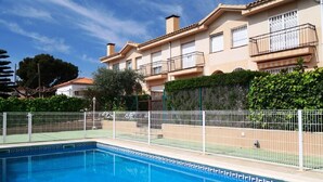Una piscina con valla blanca, rodeada por un edificio residencial con balcones y un jardín.